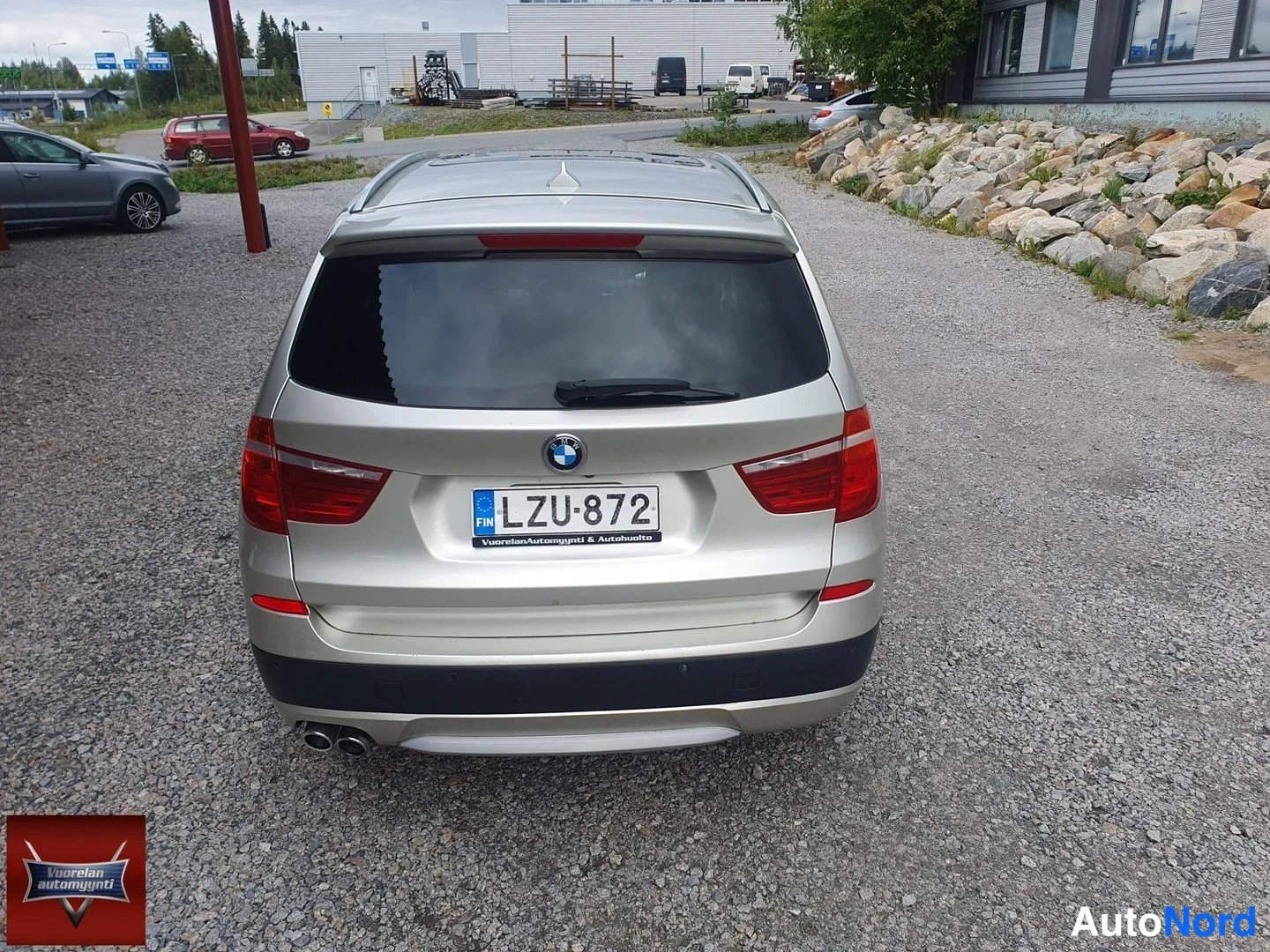 Takaa: Kultakimallemaalaatuisen BMW X3:n suora takanäkymä: tummat takavaloat, takaluukun BMW-merkki, rekisterikilpi ja kaksiosainen pakoputkisto sora-alustalla.