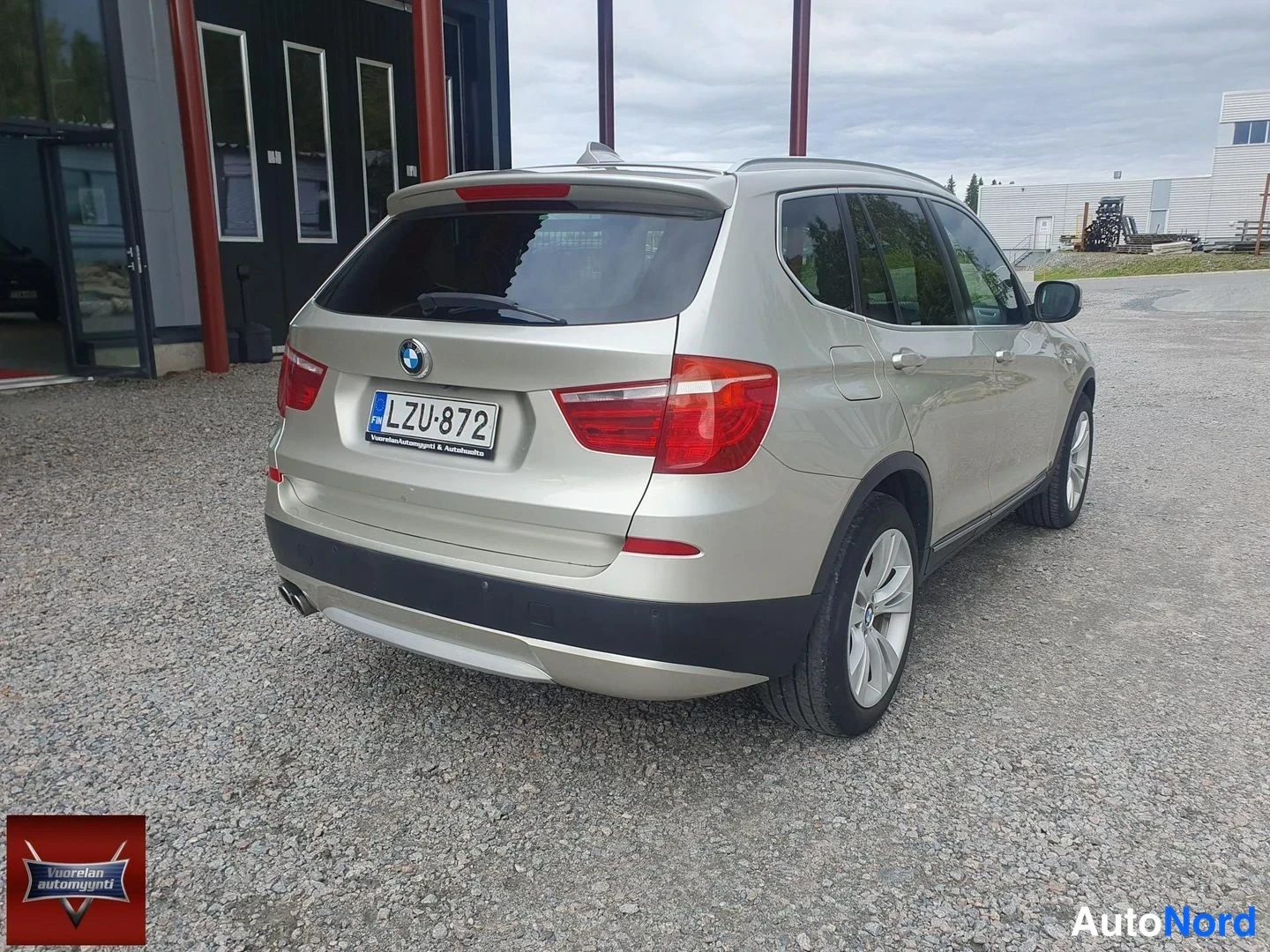 Takaviisto: Takanurkkakuva BMW X3 -maasturista: hopea kori, punaiset takavalot, rekisterikilpi ja kaksi pakoputkea sorapihalla.