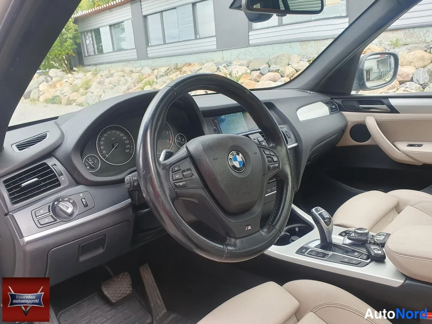 Muu: Ohjaamo vasemmalta ohjatusta autosta: BMW-ohjauspyörä M-merkillä, mittaristo, karttaa näyttävä navigointinäyttö, automaattivaihteen valitsin keskikonsolissa ja