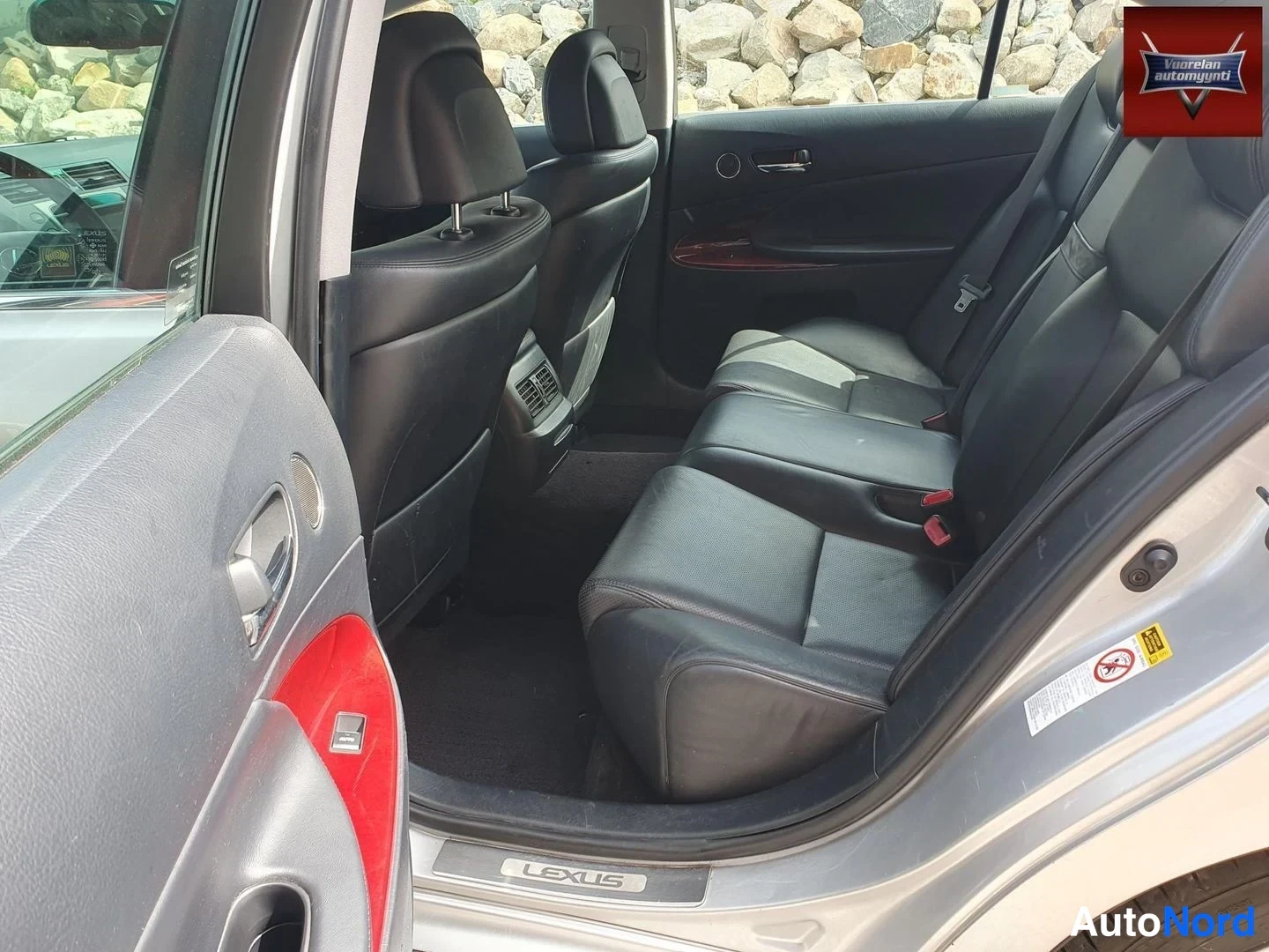Muu: Auton takaosan sisätila avoimesti takaoven kohdalta: mustat nahkaistuimet, LEXUS-tekstillä varustettu kynnyslista ja korin hopeinen runko.