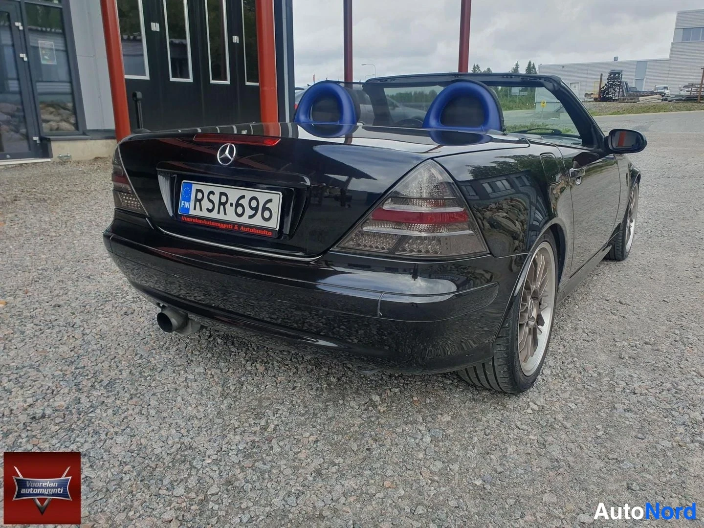 Takaviisto: Musta avoin Mercedes-Benz SLK takaa oikealta kuvattuna: rekisterikilpi, Mercedes-tähti peräluukussa, katto auki ja siniset istuimet näkyvissä.