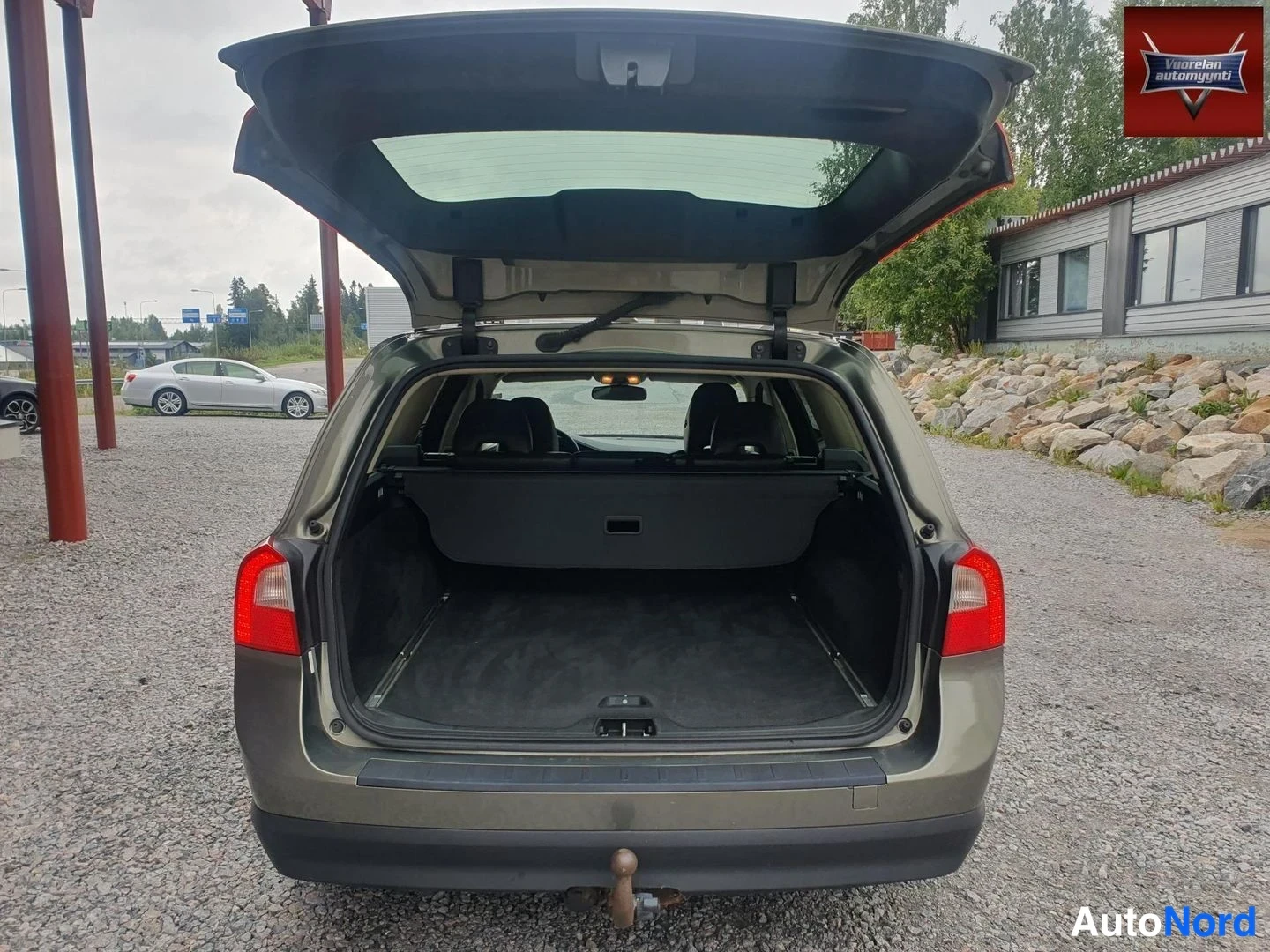 Takaa: Volvo V70 -farmurin avoin tavaratila takaa päin kuvattuna: tyhjä tumma lastitila, kuormaverho ja etuselkänojien niskatuet näkyvissä, vetokoukku takapuskurissa.