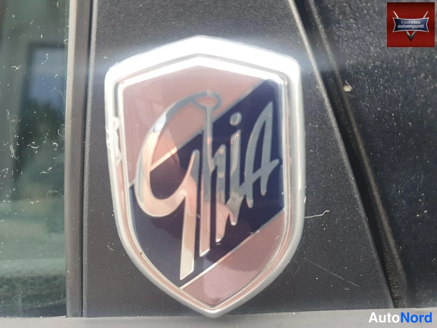 Muu: Ford Ghia -merkki tummassa b-kylkipilarissa lähikuvassa.