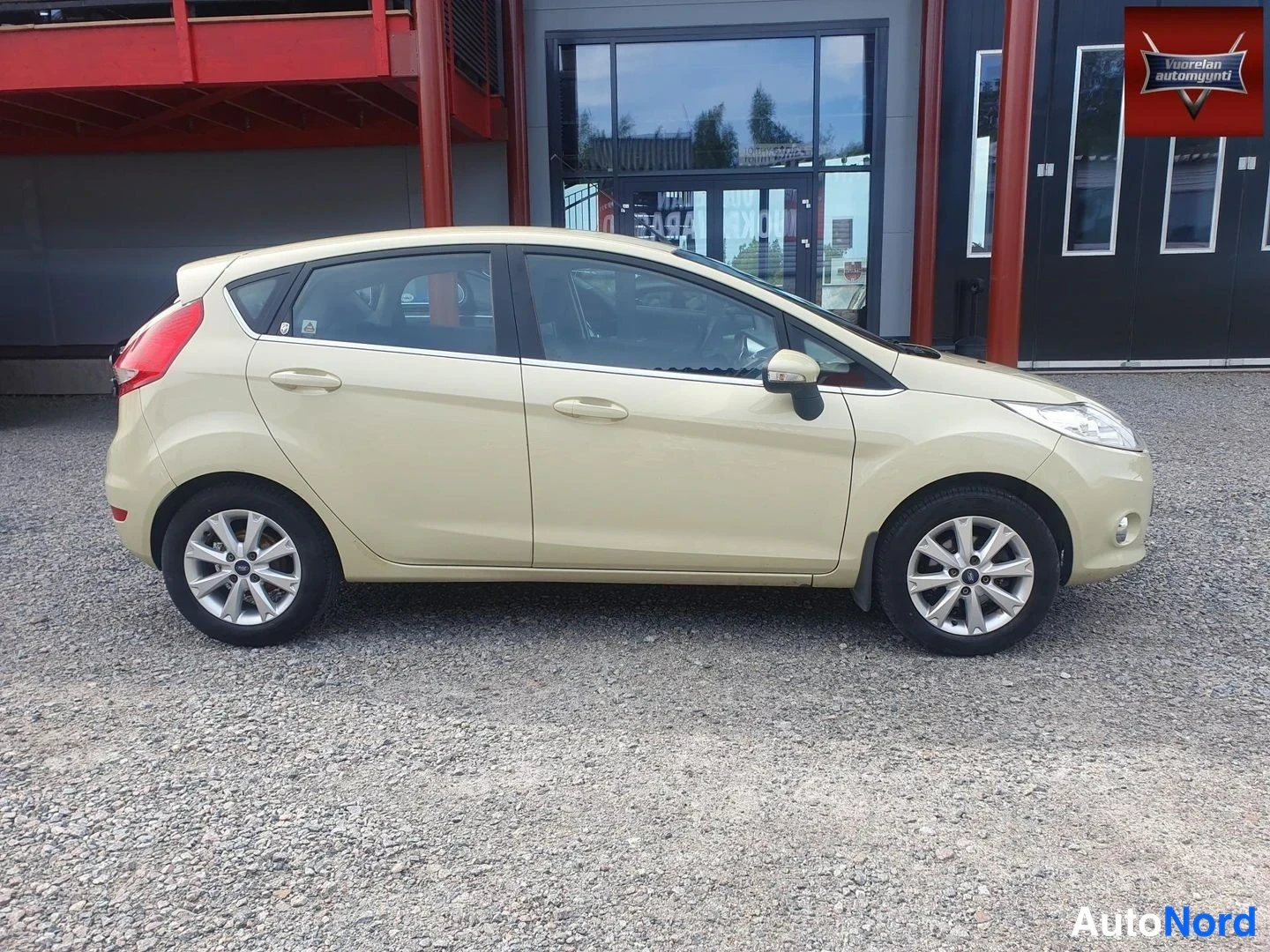 Takaviisto: Beige lavanvärinen viisiovinen hatchback sivulta oikea puoli, takapää ja takavalo näkyvät vasemmassa reunassa.
