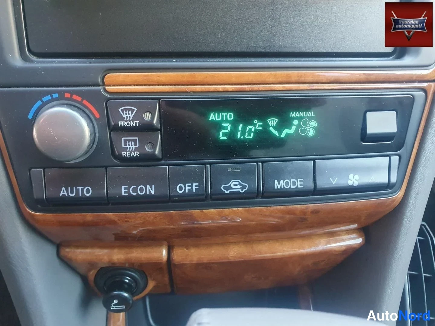 Muu: Lähikuva auton automaattisen ilmastointilaitteen hallintapaneelista: digitaalinäytössä lukee AUTO 21,0 °C ja MANUAL, painikkeina AUTO, ECON, OFF, MODE sekä tuul