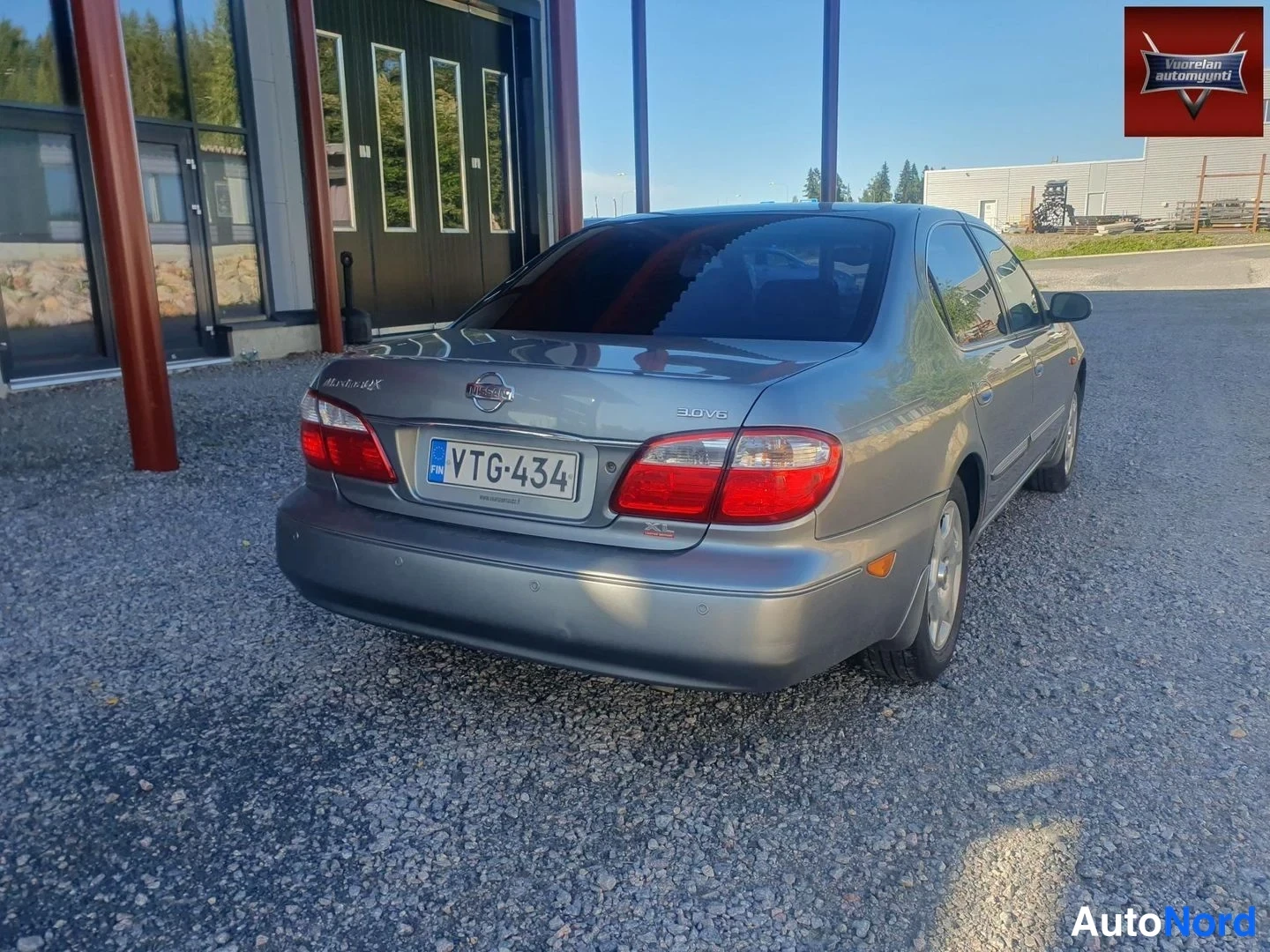 Takaviisto: Hopeanharmaa Nissan Maxima QX 3.0 V6 -sedan takakulmakuvassa; takavalot, Nissan-merkki, 3.0 V6 -merkki ja rekisteritunnus näkyvissä, auton vasen sivu sivuprofii