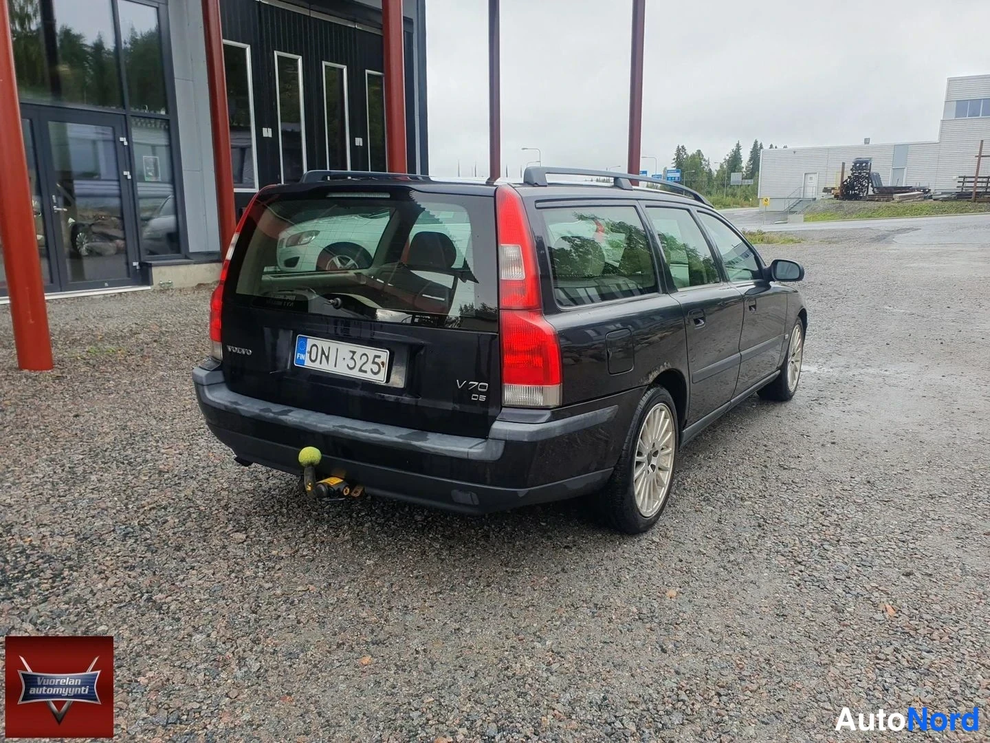 Takaviisto: Takaa sivulta kuvattu musta Volvo V70 -farmari, jonka rekisterikilpi on; katolla kattokaiteet ja takapuskurin alla vetokoukku keltaisella kytkinpallolla.