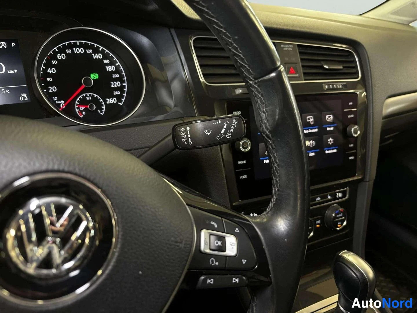 Muu: Ohjaamon sisäkuva: rattisignaalikahva ja kojelaudan mittarit, Volkswagen-merkki rattiin, keskibrändin kosketusnäyttö ja ilmastointilaitteen säätimet.
