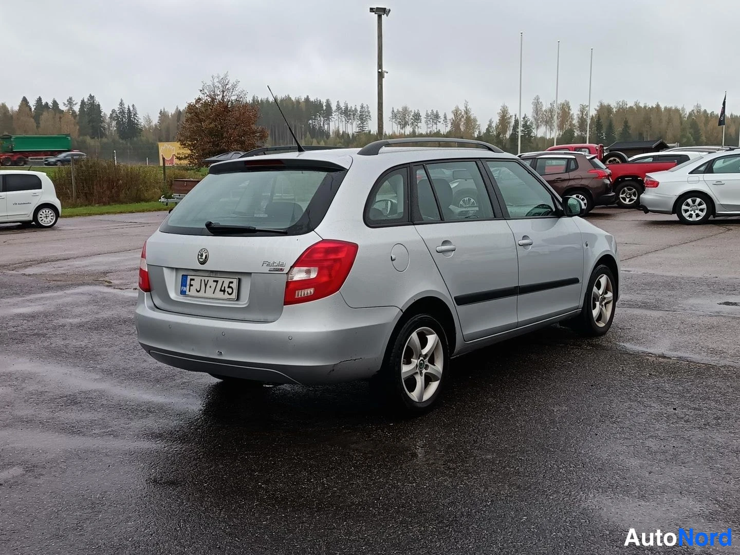 Takaviisto: Hopeanvärinen farmariauto takakulmasta, rekisteritunnus F JY-745, takaluukussa Fabia-teksti, kostealla parkkialueella.