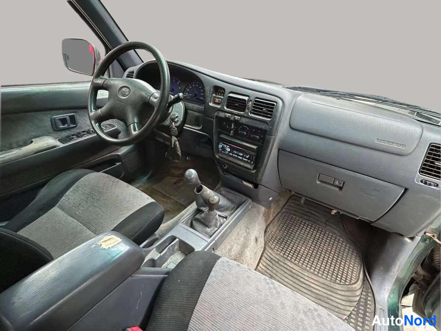 Muu: Ohjaamo vasemmalta: tumma kojelauta, Toyota-ohjauspyörä, manuaalivaihteen keppi ja radioinstrumentit.