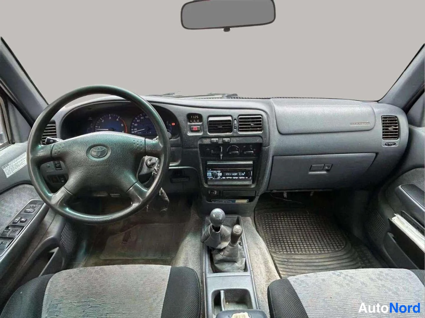 Muu: Ohjaamo edestä: Toyota-merkkinen ohjauspyörä, kojelauta ja manuaalivaihteisto.