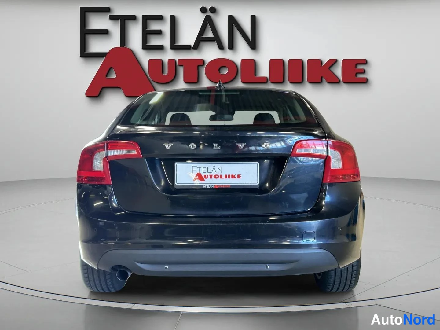 Takaa: Tummansinisen sedan-auton suora takanäkymä, näkyvät takavalot, VOLVO-merkintä ja takapuskuri studiossa.