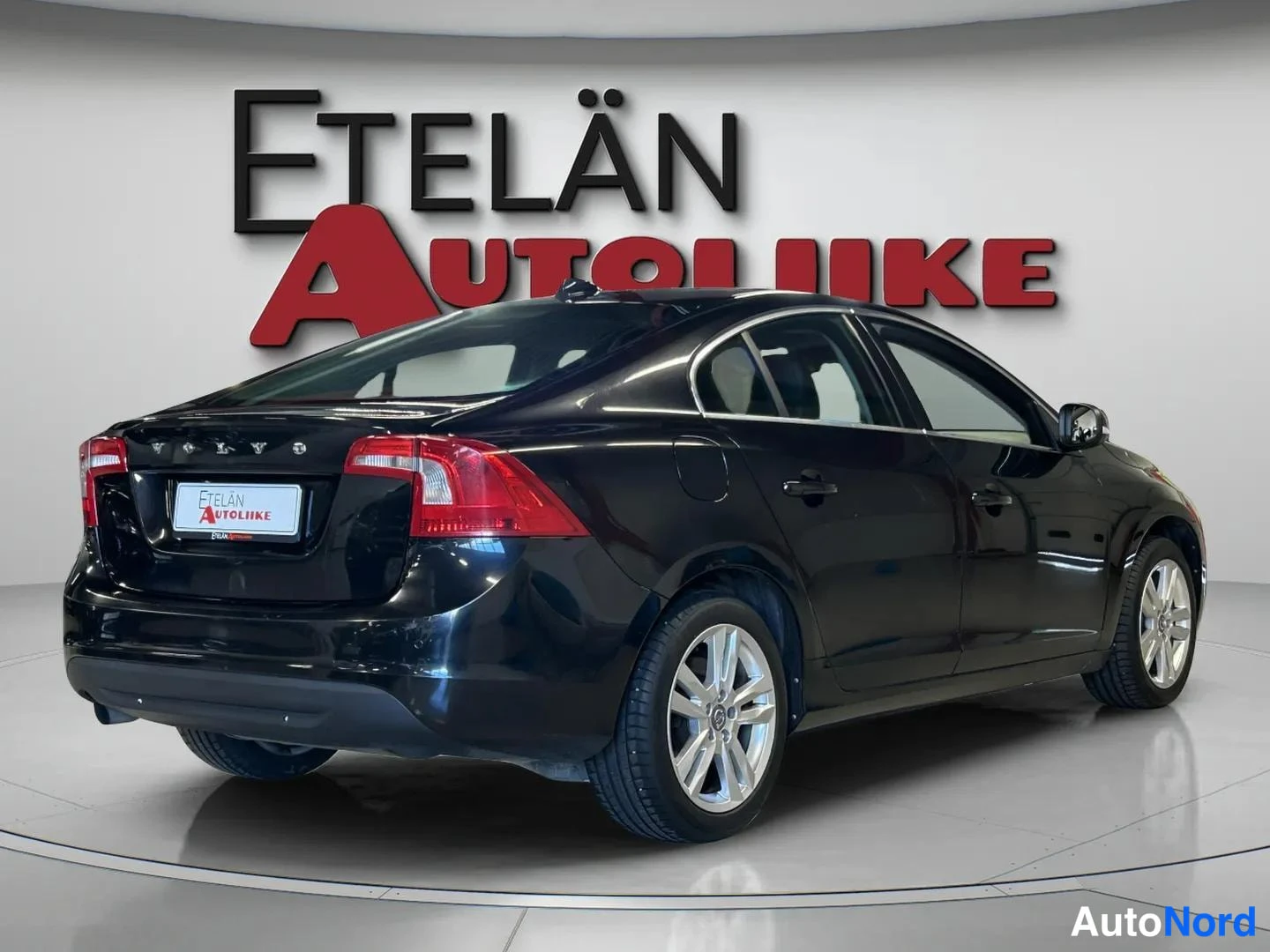 Takaviisto: Mustan sedan-auton takakulmanäkymä vasemmalta, näkyvät takavalot, VOLVO-merkintä ja vasen kylki studiossa.