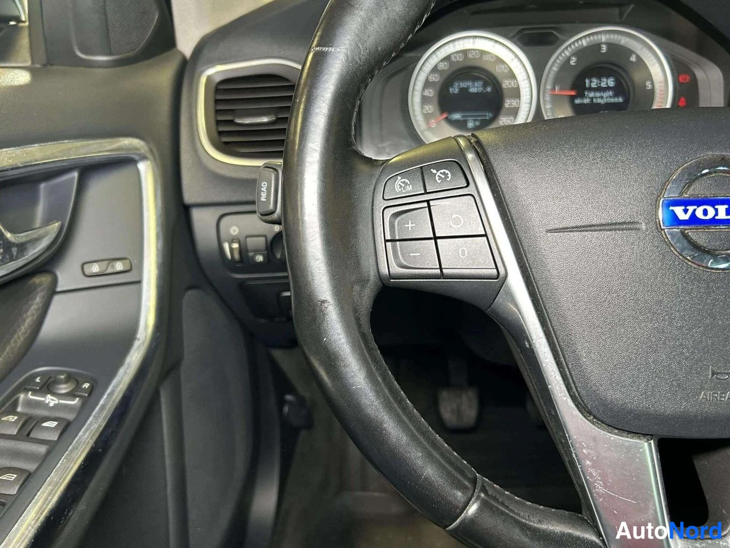 Muu: Volvo-merkillä varustettu ohjauspyörä ja mittaristo, kellonaika 12:26 kojelaudan näytöllä.
