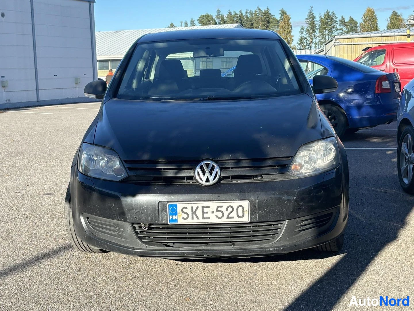 Edestä: Mustan henkilöauton etukuva suoraan edestä; rekisterikilpi, VW-merkki etusäleikössä.