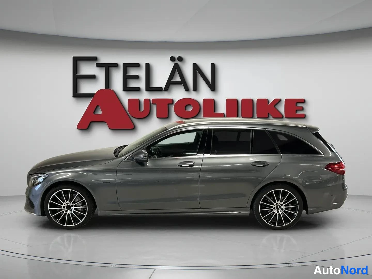 Sivulta: Tummanharmaan Mercedes-Benz C-luokan farmarin sivukuva suoraan sivulta, oikea kyljä näkyvissä.