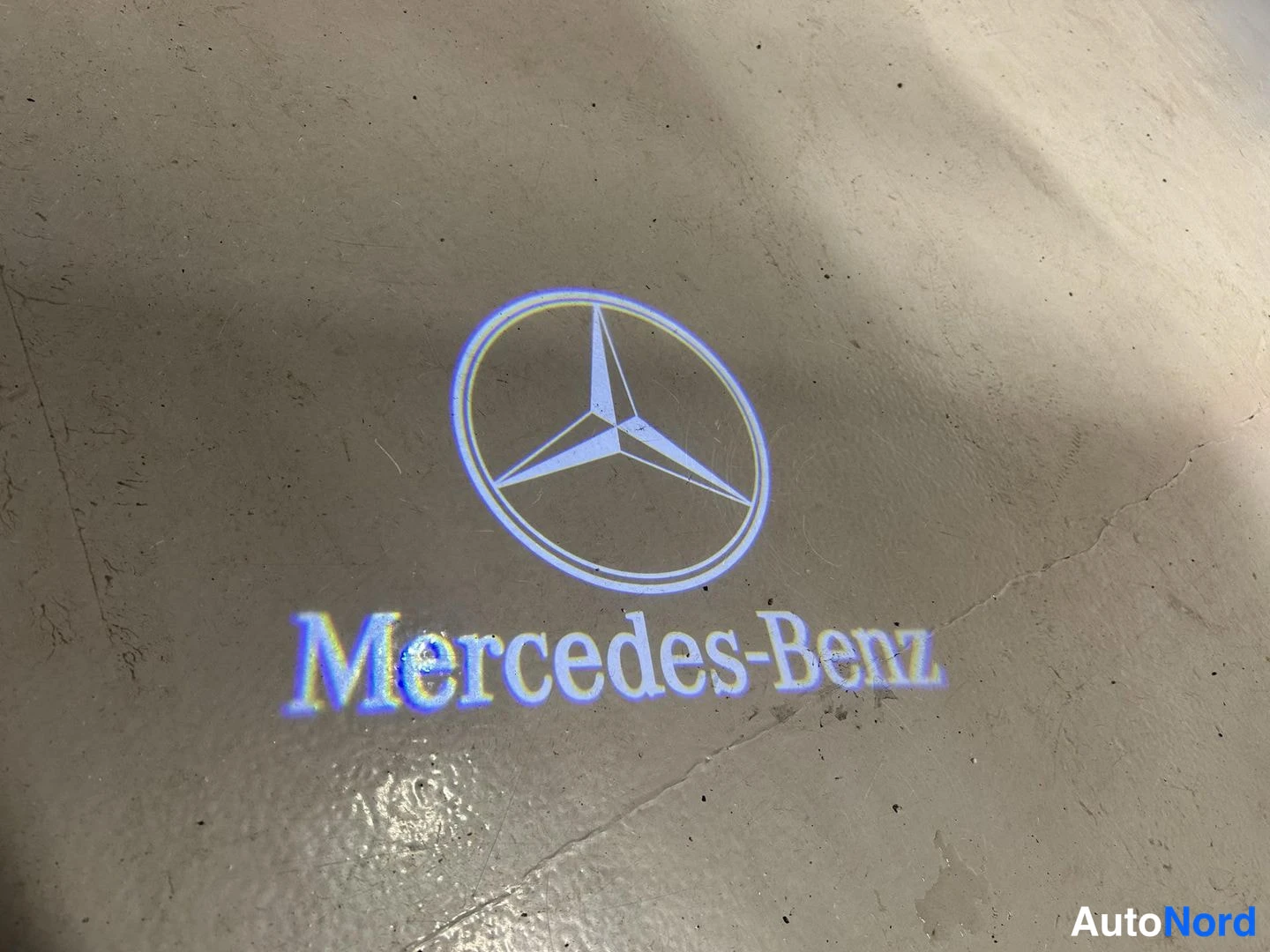 Muu: Projektori valaisee Mercedes-Benz-logon ja tekstin Mercedes-Benz maahan lattialle.