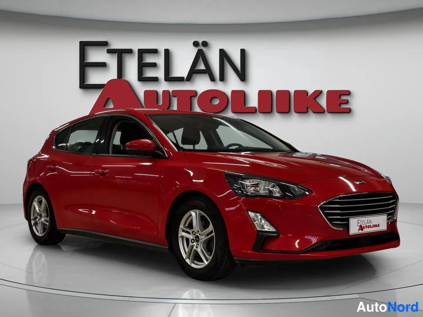 Etuviisto, nokka oikealle: Punainen viistosti edestä oikealta kuvattu automobiili studioympäristössä, Etelän Autoliike -logo taustalla.