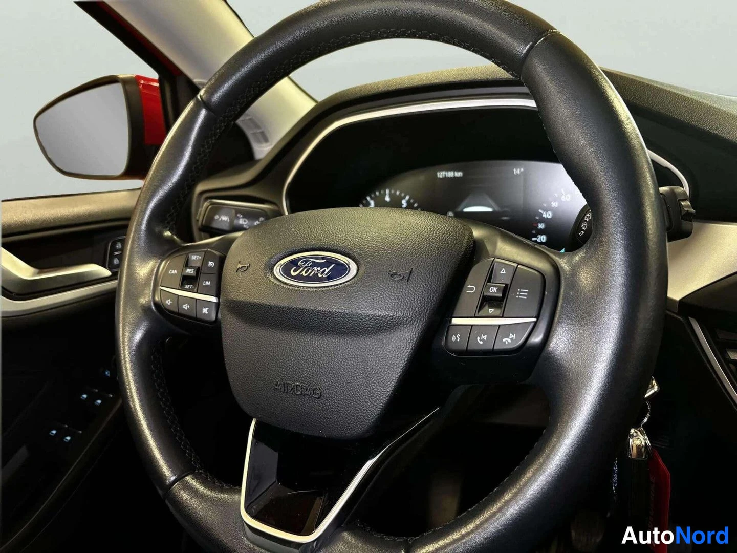 Muu: Ford-merkkinen ohjauspyörä monitoiminapeilla, takana osittain näkyvä digitaalinen mittaristo ja punainen sivupeili.