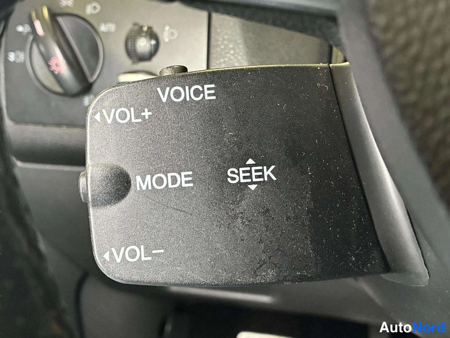 Yksityiskohta: Ohjauspyörän ääniohjaus- ja äänenvoimakkuusvipu, jossa tekstit VOICE, VOL+, MODE, SEEK ja VOL-.