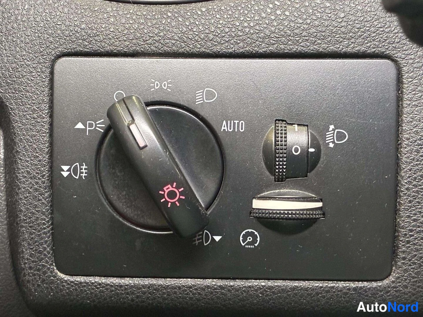 Yksityiskohta: Valojen ja suuntavilkkujen kytkinpaneeli: AUTO-merkitty valokytkin, sumuvalokytkin ja säätörulla.
