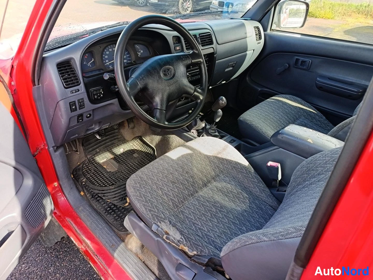 Muu: Auton sisätila kuljettajan ovesta kuvattuna: kaksi etupenkkaa, Toyota-merkitty ratti, mittaristo ja manuaalivaihteen vaihdekeppi.