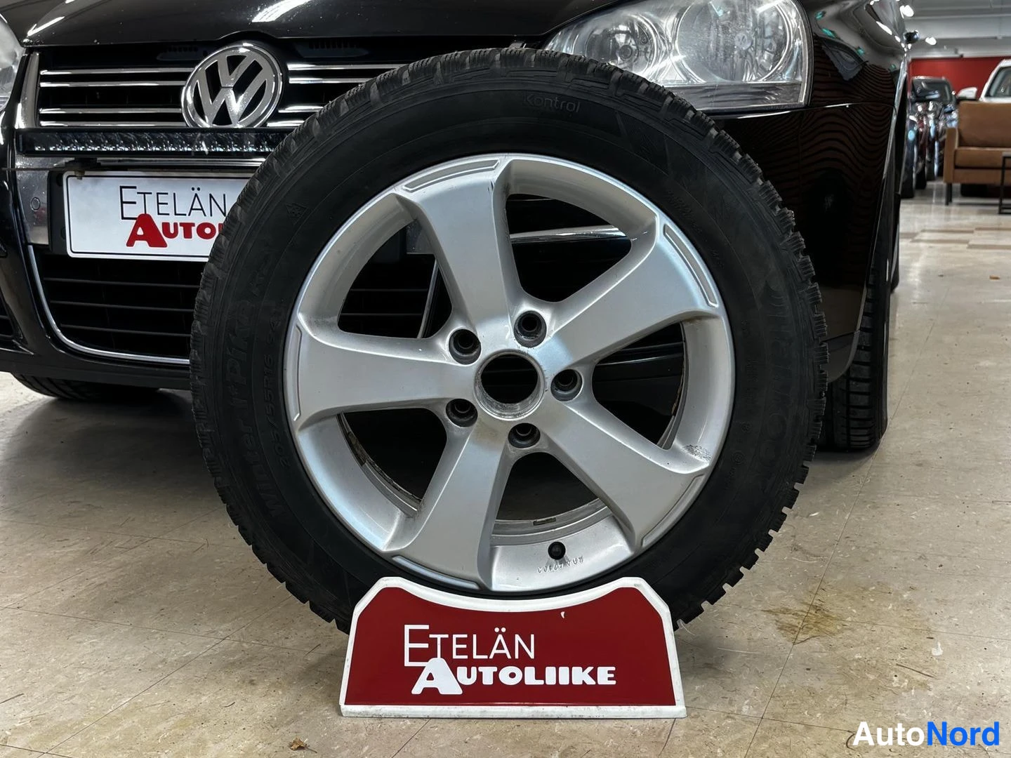 Muu: Auton keula VW-merkillä ja kokoonpanossa oleva talvirengas hopeavannella Etelän Autoliike-nimikyltillä.