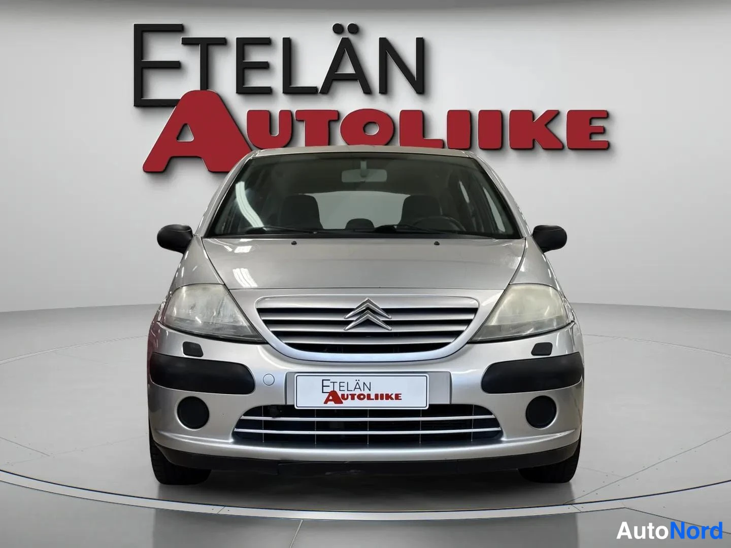 Edestä: Hopeanvärinen Citroen C3 suoraan edestä kuvattuna autonliikkeen studiotaustaa vasten.