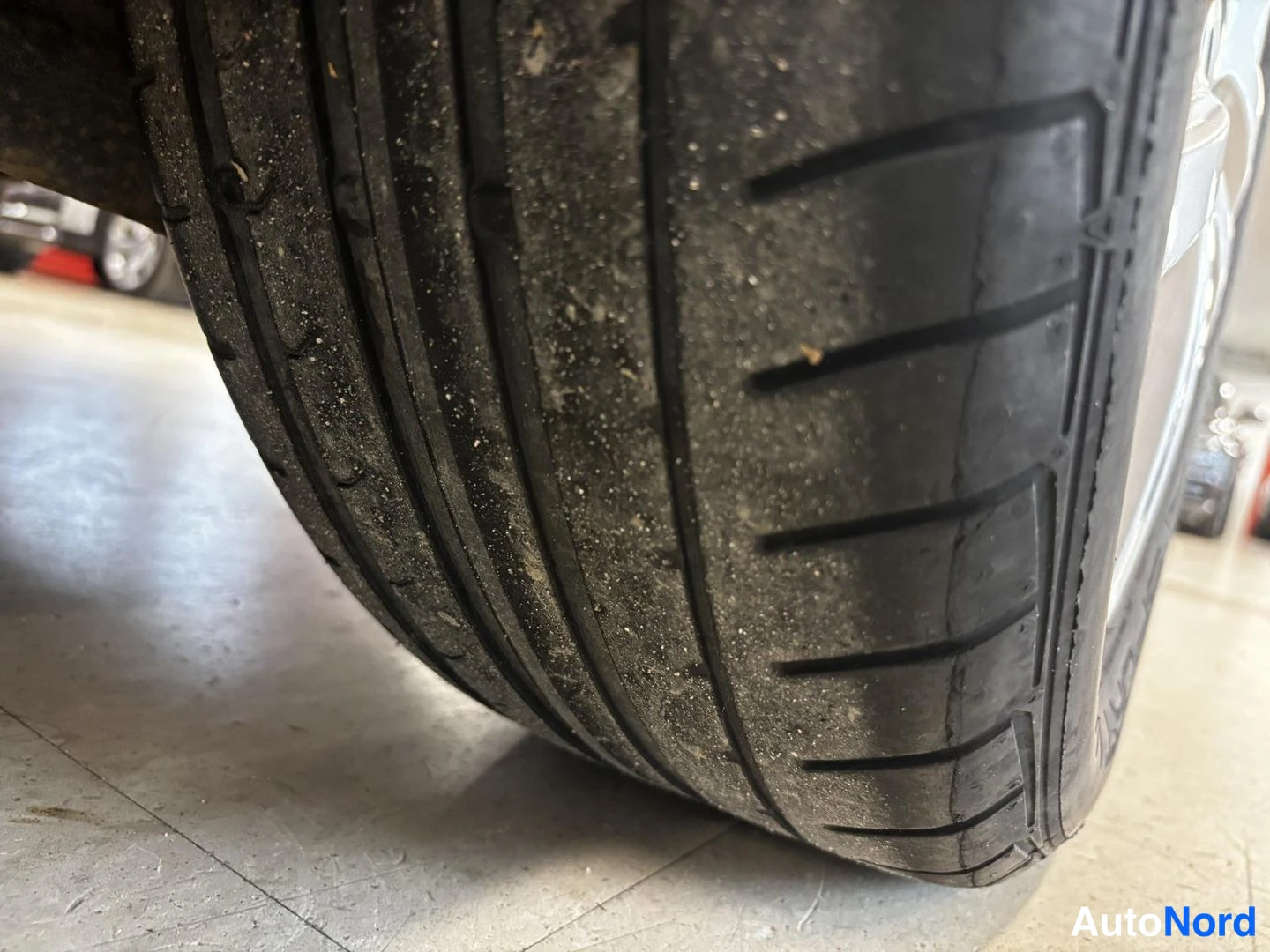 Yksityiskohta: Lähikuva auton renkaasta, jossa näkyy urat ja pinnan lika hallitilassa.