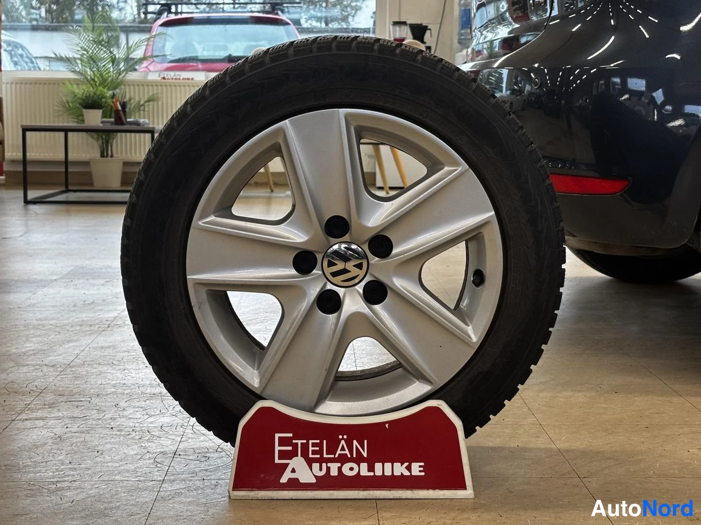 Yksityiskohta: Hopeinen Volkswagen-kehälevy talvirenkaalla näyttelytelineessä autoliikkeen tiloissa.
