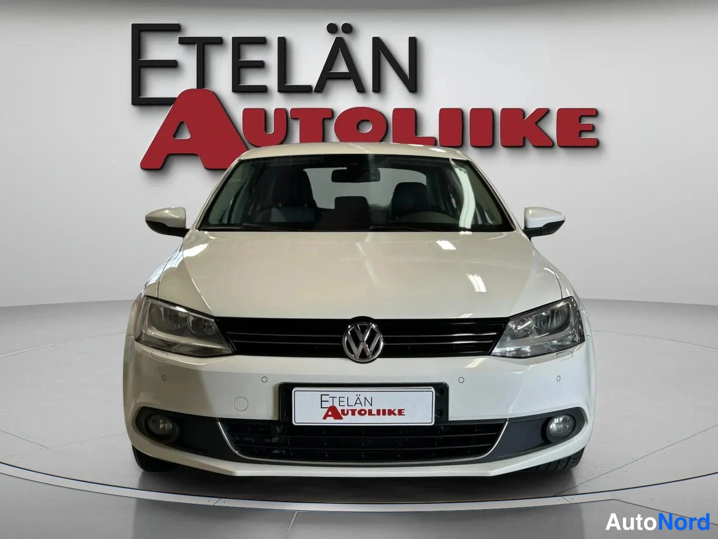 Edestä: Valkoisen Volkswagen Jetta -sedan etunäkymä, etusäleikkö, ajovalot ja VW-merkki näkyvät.