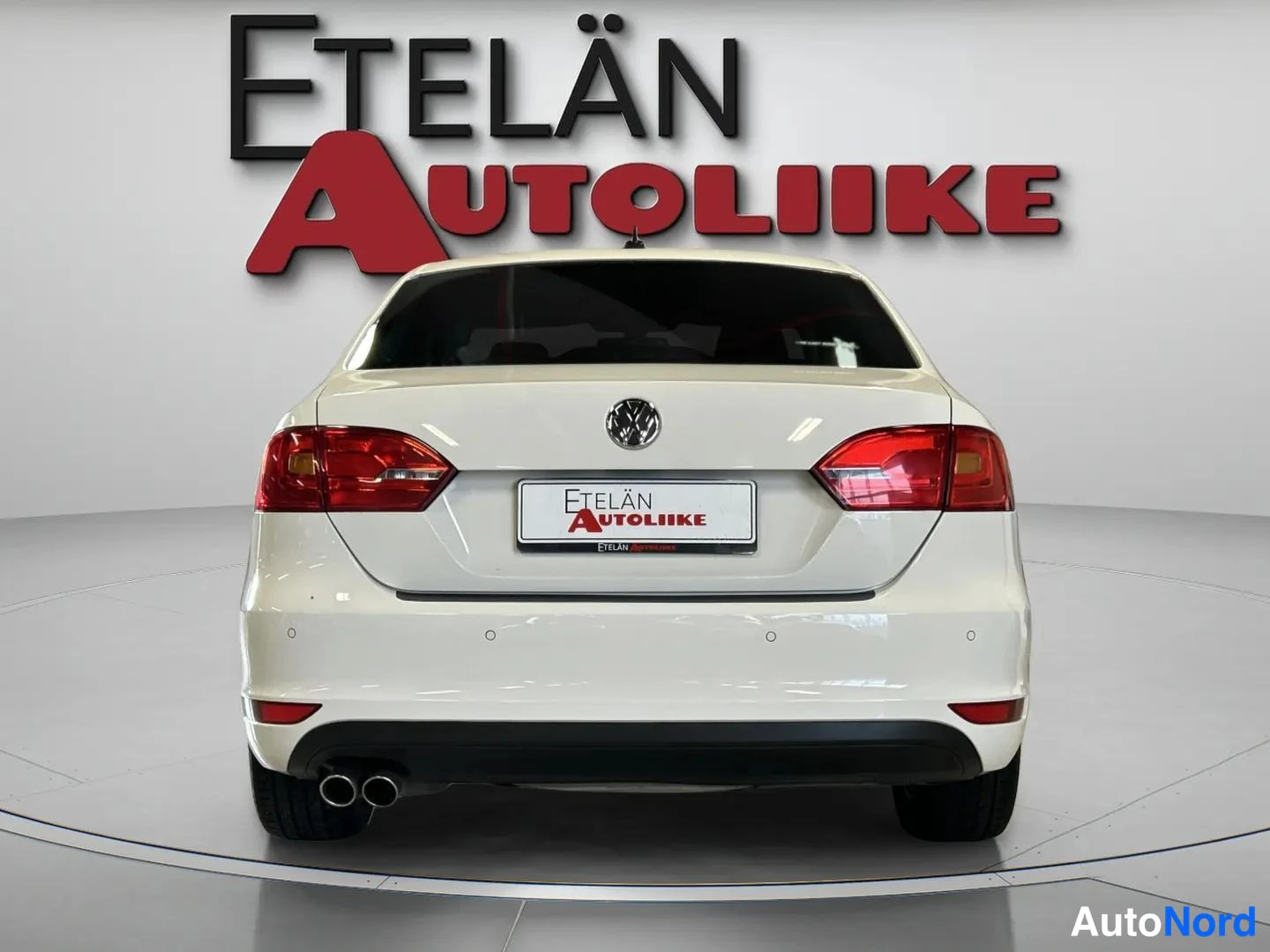 Takaa: Valkoinen sedan suoraan takaa: punaiset takavalot, VW-merkki ja tuplapakoputki näkyvät.