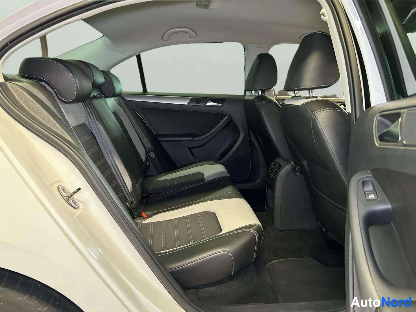 Takaistuimet: Back seats from the right rear door showing a three-seat bench. Black leather bolsters and headrests frame light grey fabric inserts with white contrast stitchi