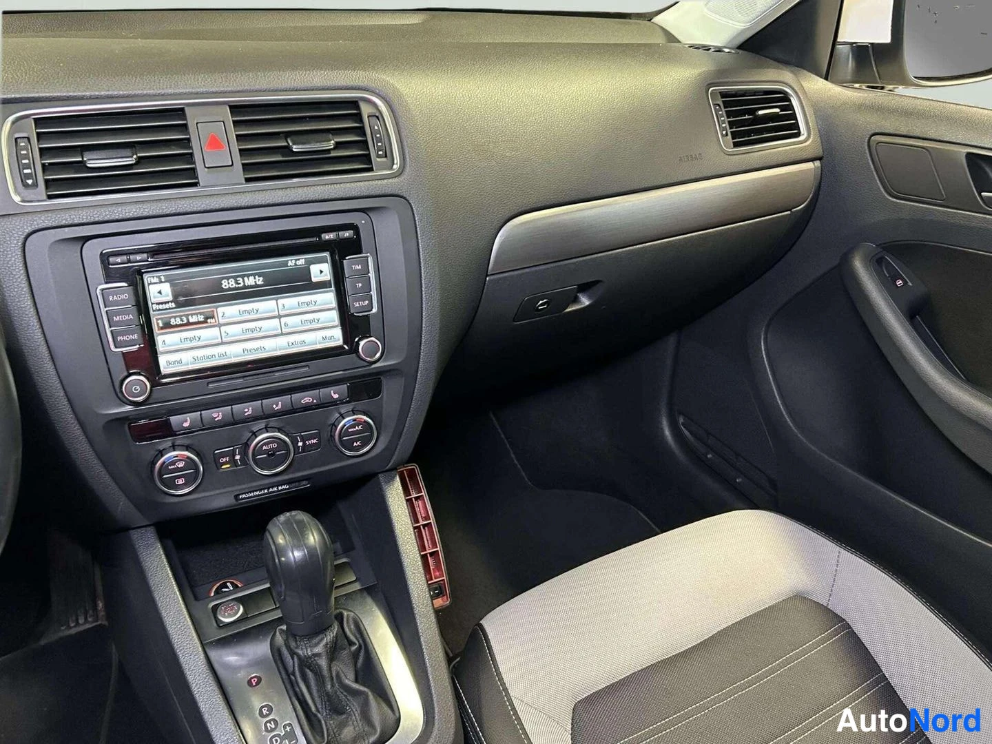 Edestä: Volkswagenin ohjaamo vasemmalta: tumma kojelauta, radio-näyttö, ilmastointipaneeli ja kaksivärinen istuin.