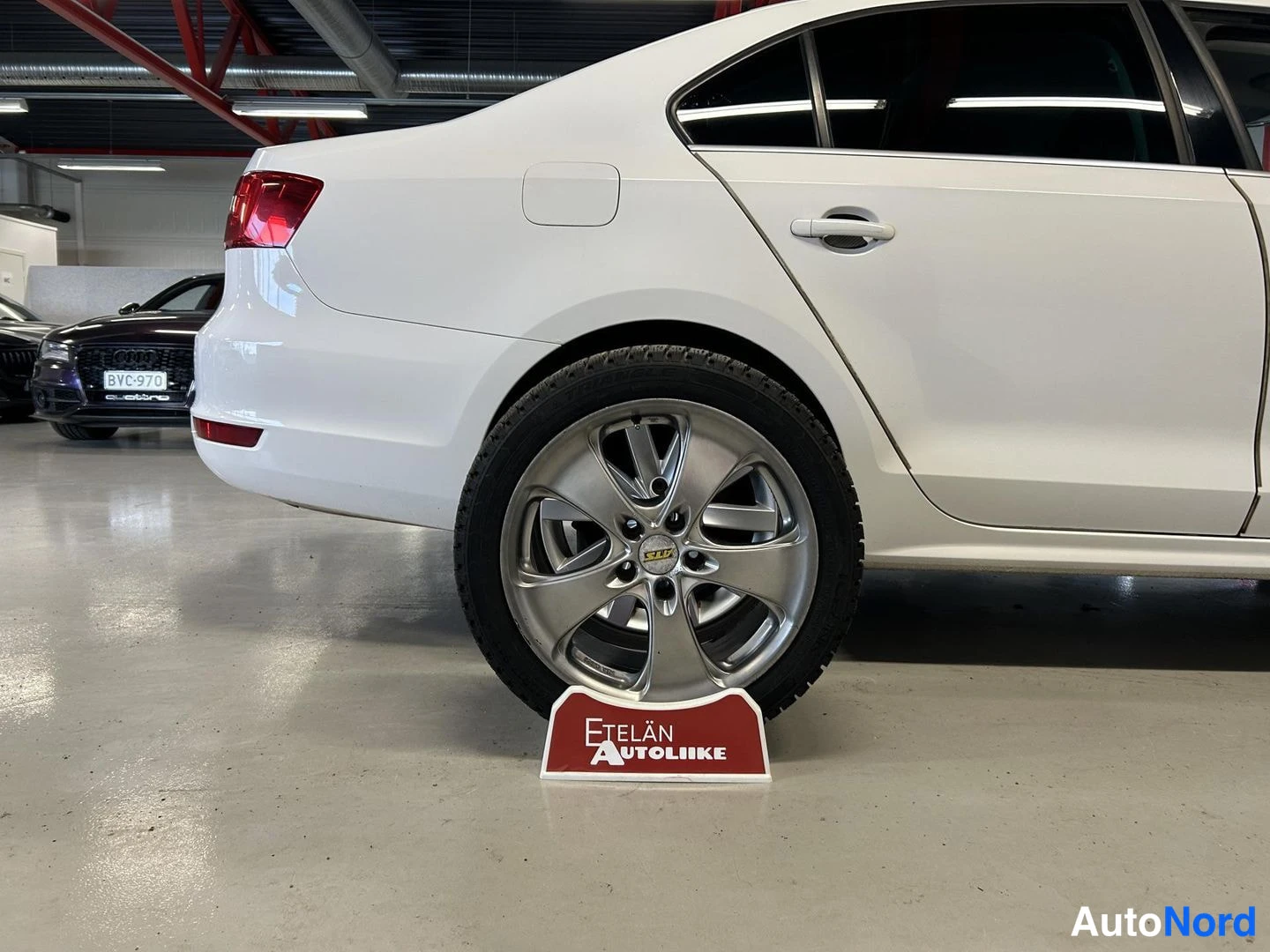 Takaviisto: Rear three-quarter view of white sedan parked in indoor facility.