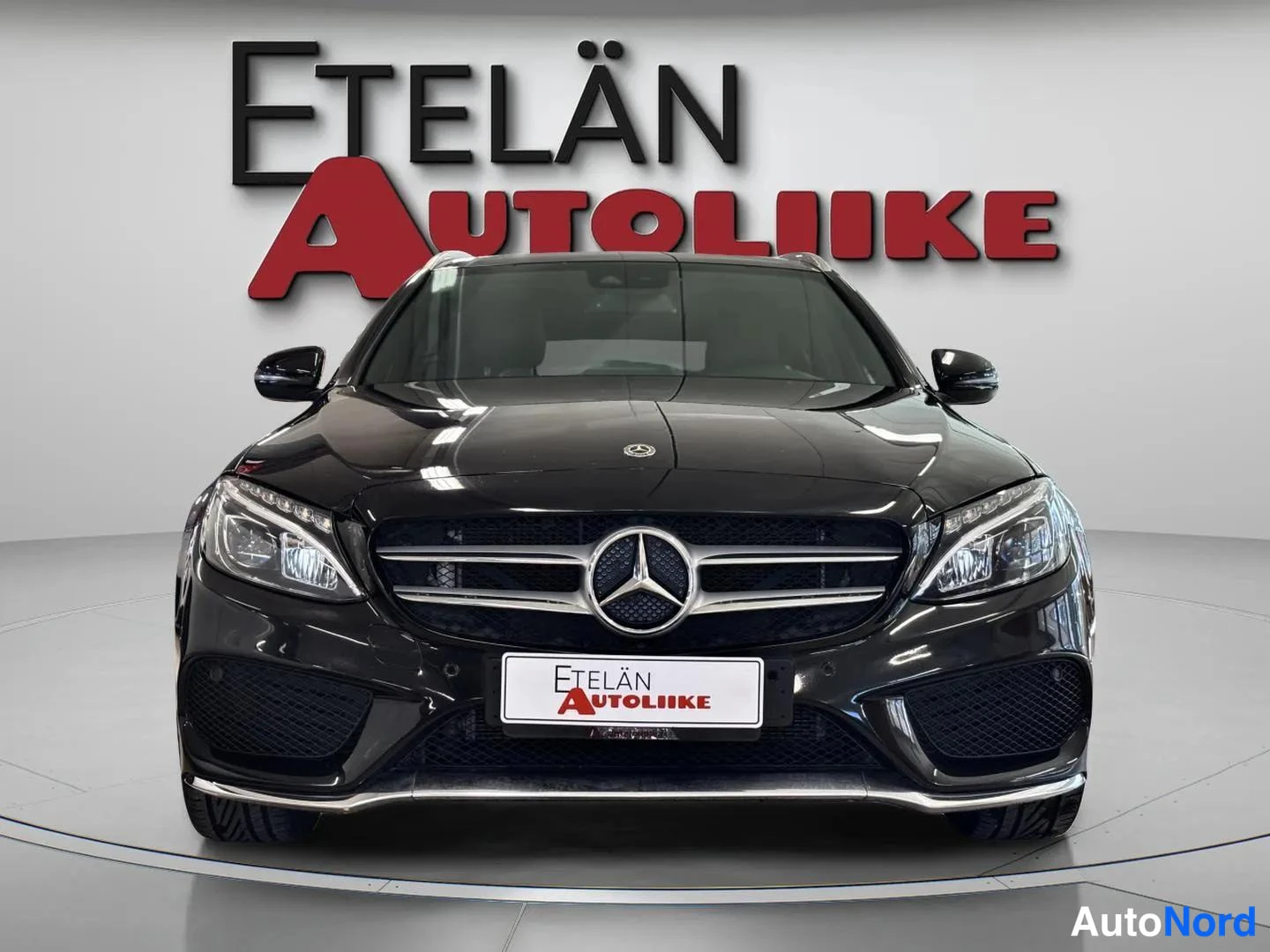 Edestä: Mustan Mercedes-Benzin etupää suoraan edestä: etusäleikkö Mercedes-tähdellä, ajovalot ja Etelän Autoliike -kyltti rekisterin paikalla.