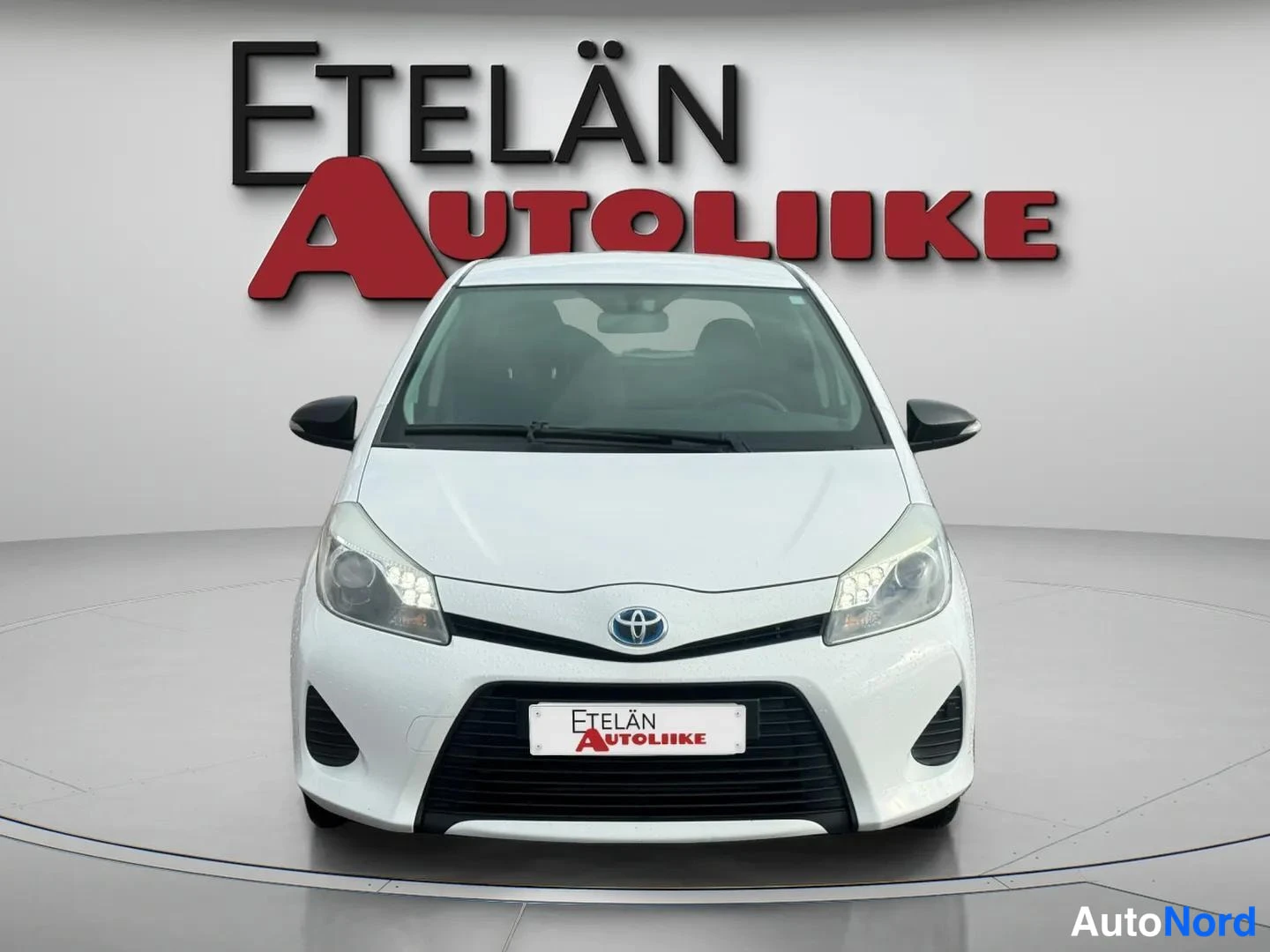 Edestä: Valkoinen Toyota Yaris etupäästä kuvattuna studioympäristössä.