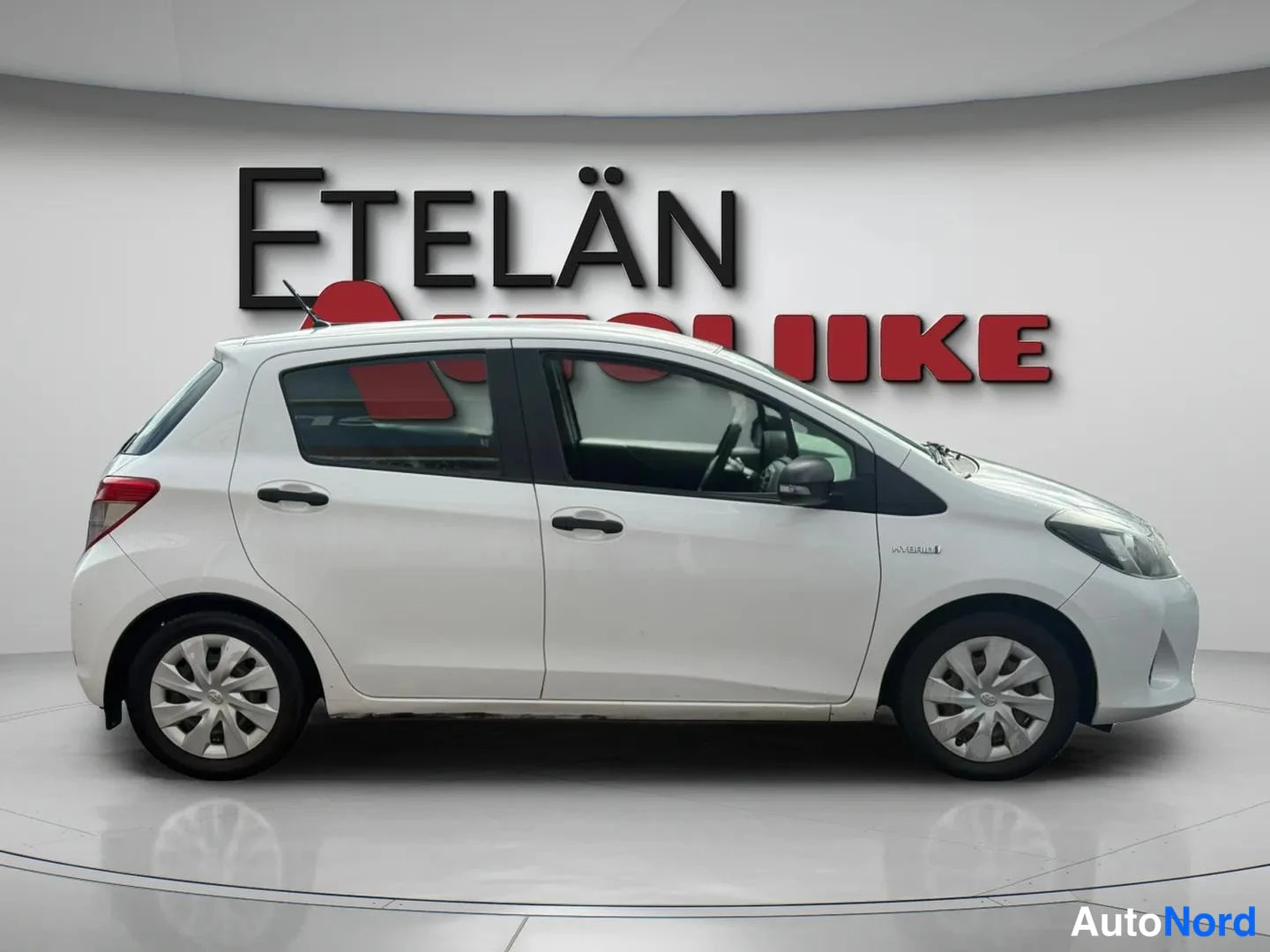 Sivulta: Valkoinen Toyota Yaris sivulta oikealta kuvattuna, kylki ja yksi ovi näkyvissä.