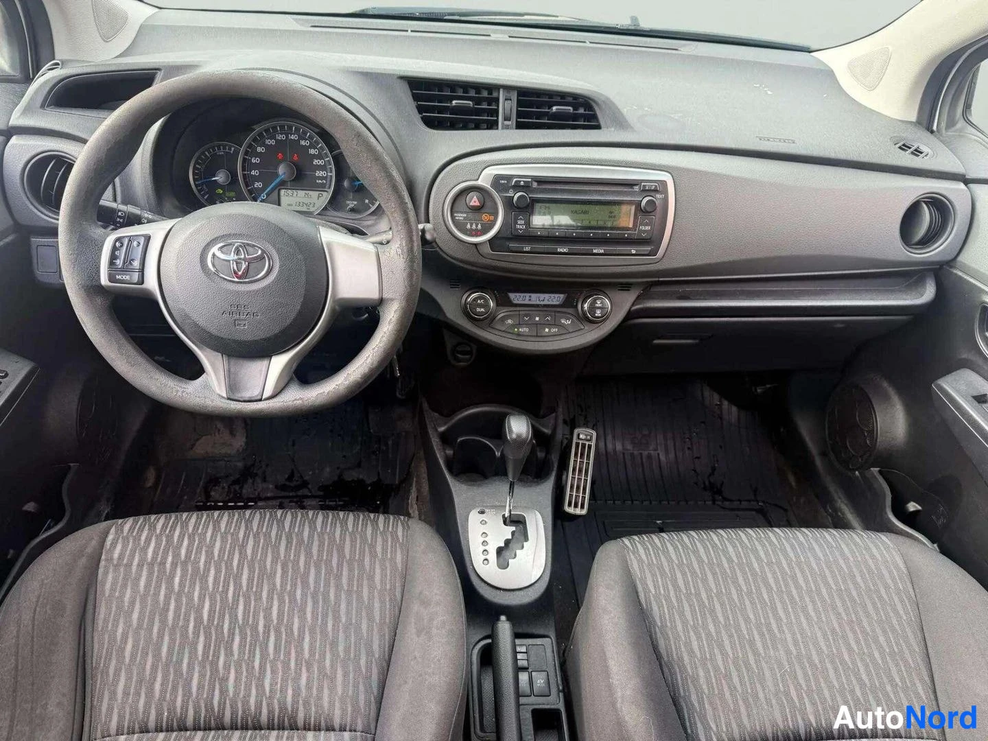Muu: Toyota-henkilöauton ohjaamo suoraan edestä: Toyota-merkkinen ohjauspyörä, kojelauta ja radio- ja ilmastointilaitteet A/C-painikkeella, automaattivaihteiston val