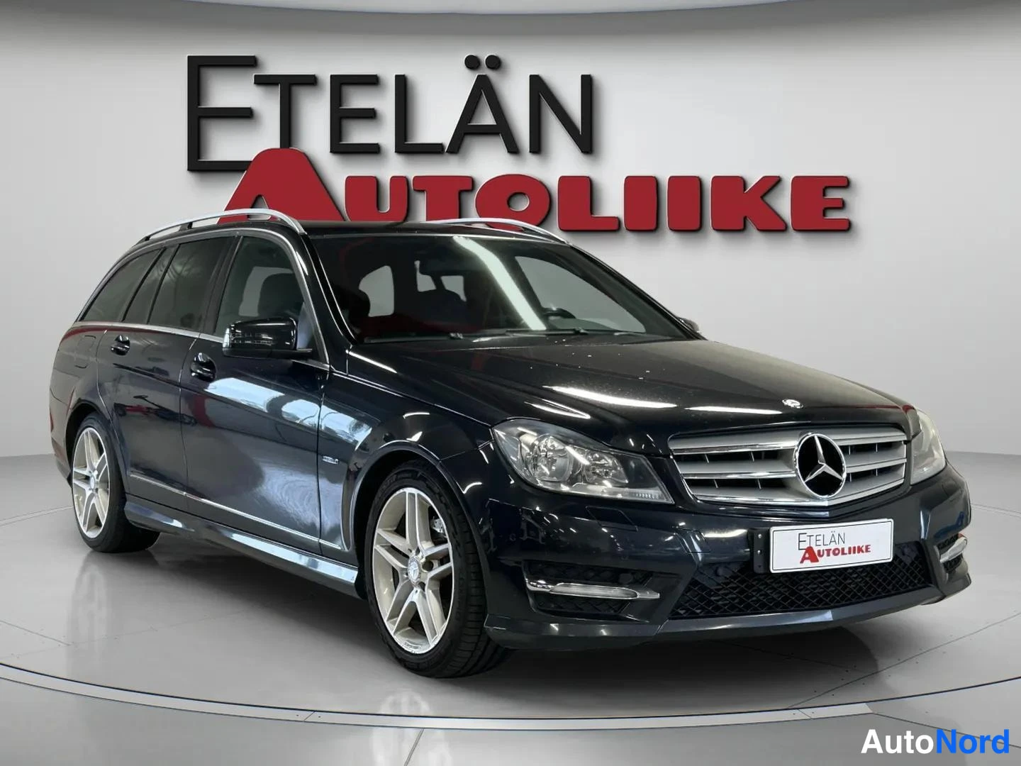 Etuviisto, nokka oikealle: Musta Mercedes-Benz C-sarjan farmariauto kuvattu kolmannes kulmasta edestä, keula oikealla; etusäleikkö ja merkki, sumuvalot, kattokaiteet ja moniosaiset
