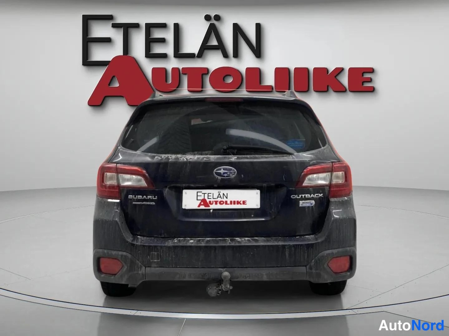 Takaa: auton takaosa, takamootti ja takapuskuri, takaluukun OUTBACK-merkintä, vetokoukku takapuskurin alla, harmaa tausta, Etelän Autoliike-logo taustalla, harmaa latt
