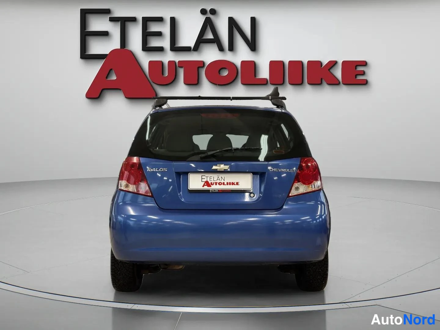 Takaa: Sininen Chevrolet Kalos -henkilöauto suoraan takaa kuvattuna; takaluukissa Chevrolet-merkintä ja kattokaiteet katolla.