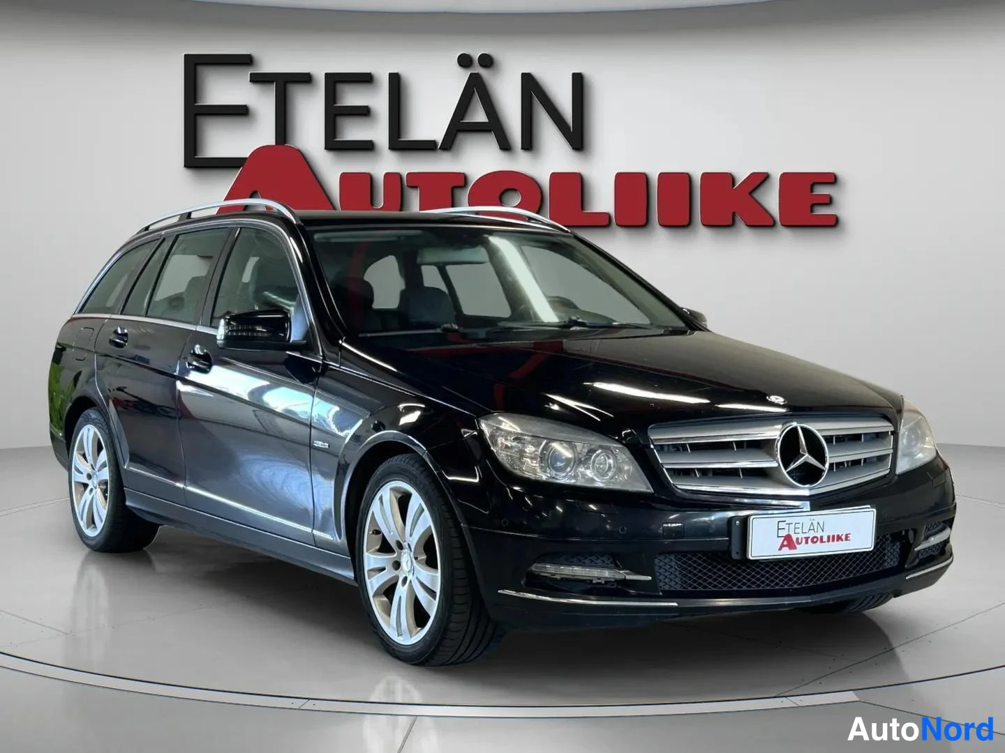 Etuviisto, nokka oikealle: Mercedes-Benz C -farmari etuylänurakka oikealta, musta, katettu näyttelytilassa