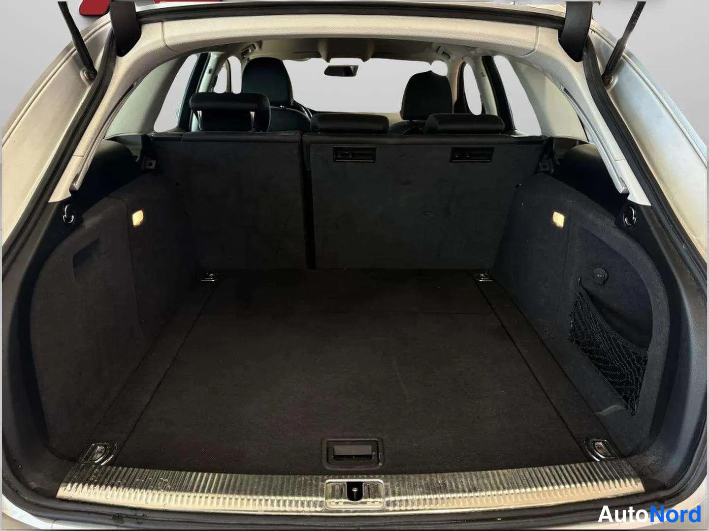 Muu: Audi A4 Avantin avattu tavaratila: tumma verhoilu, taitettu takapenkki ja joustoverkko oikealla sivulla.