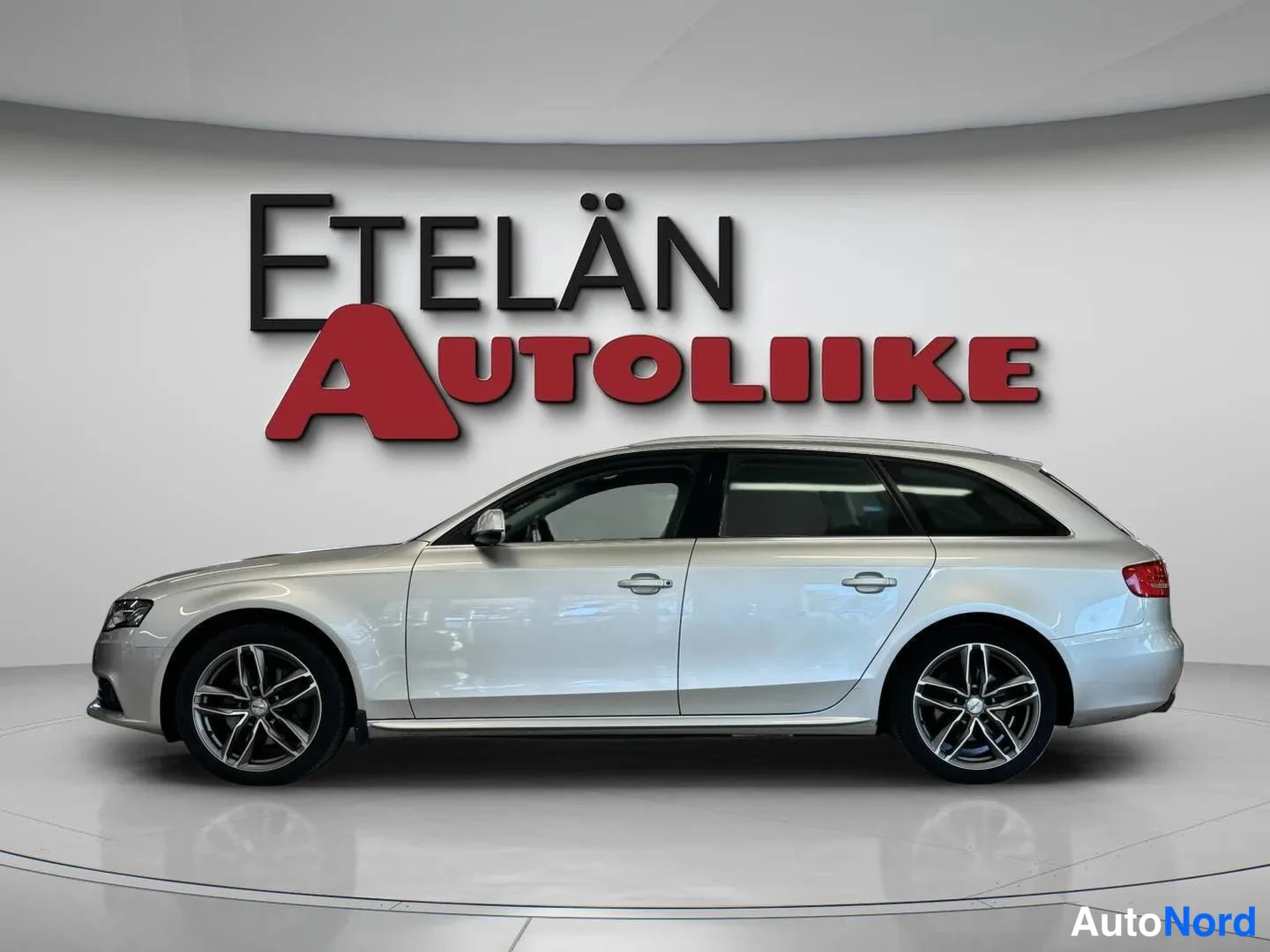Sivulta: Profile view of a silver station wagon showing one side profile, alloy wheels, and roof rails against a white background
