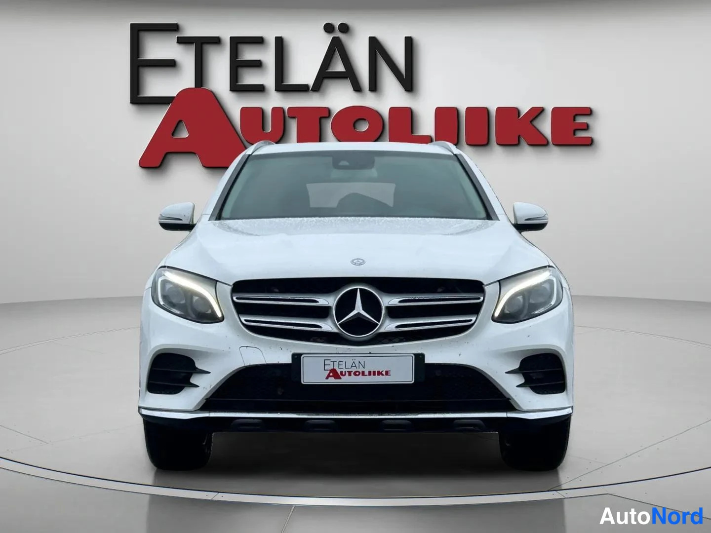 Edestä: Valkoinen Mercedes-Benz GLC edestä päin kuvattuna, keskellä Mercedes-tähti ja kromikehyksinen etusäleikkö, molemmin puolin autonvalot.