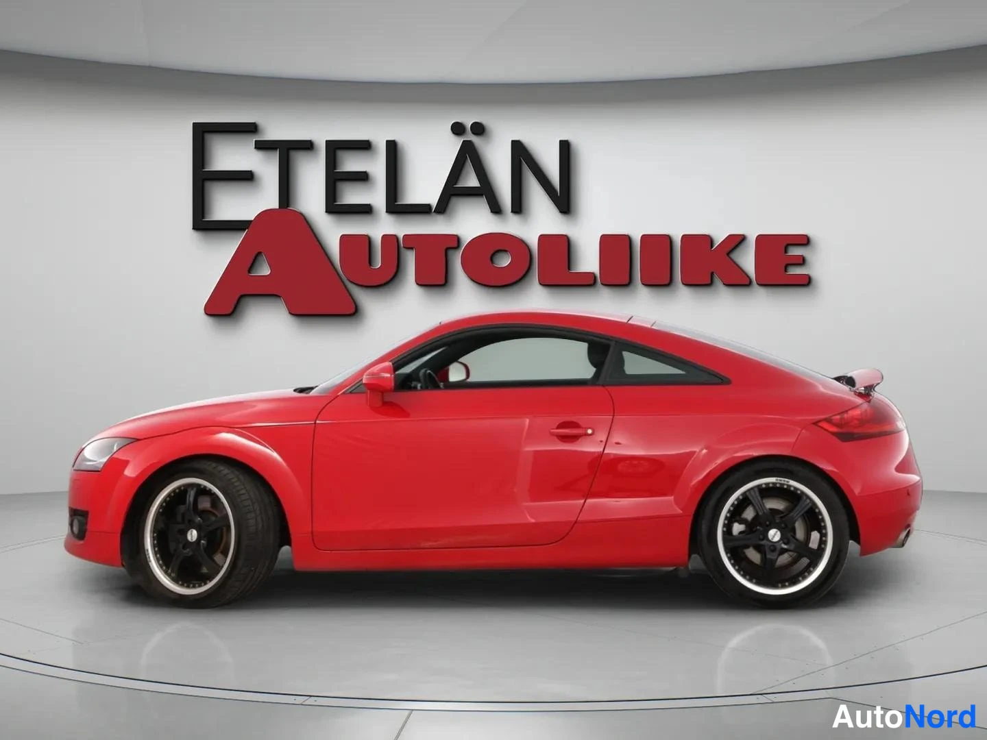 Sivulta: Punaisen Audi TT Coupén sivukuva studiossa, oikeanpuoleinen kylki ja kolme ovea näkyvät.