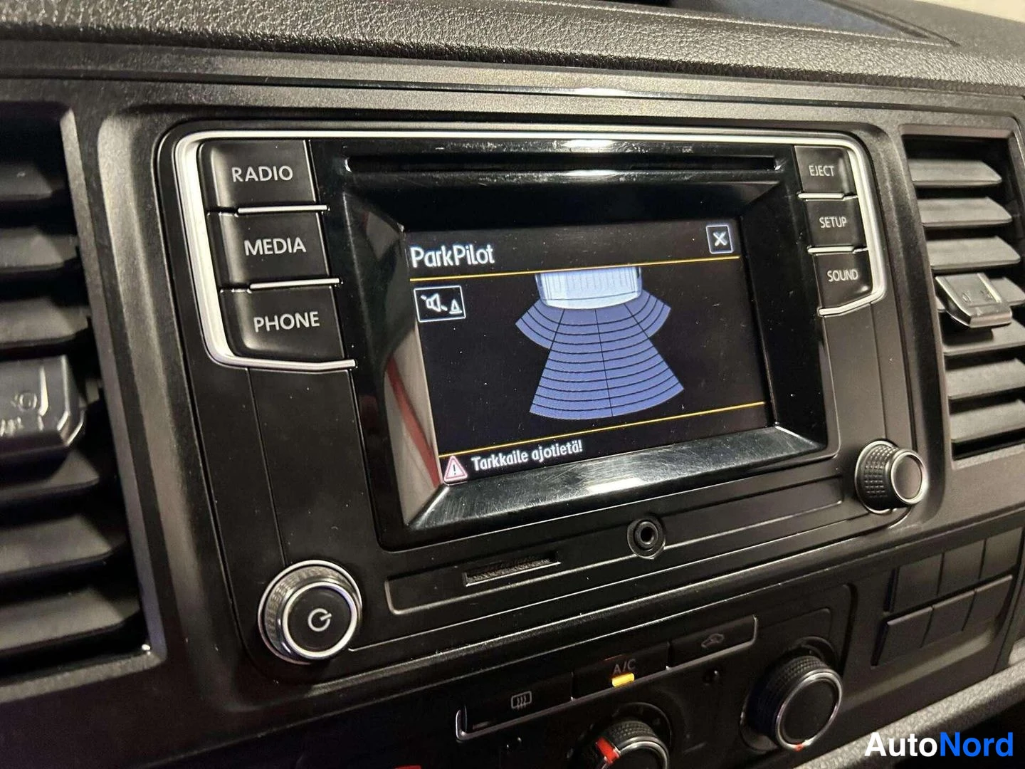 Muu: Radiot: näytöllä ParkPilot ja teksti 'Tarkkaile ajotietä', näppäimet Radio, Media, Phone, A/C.
