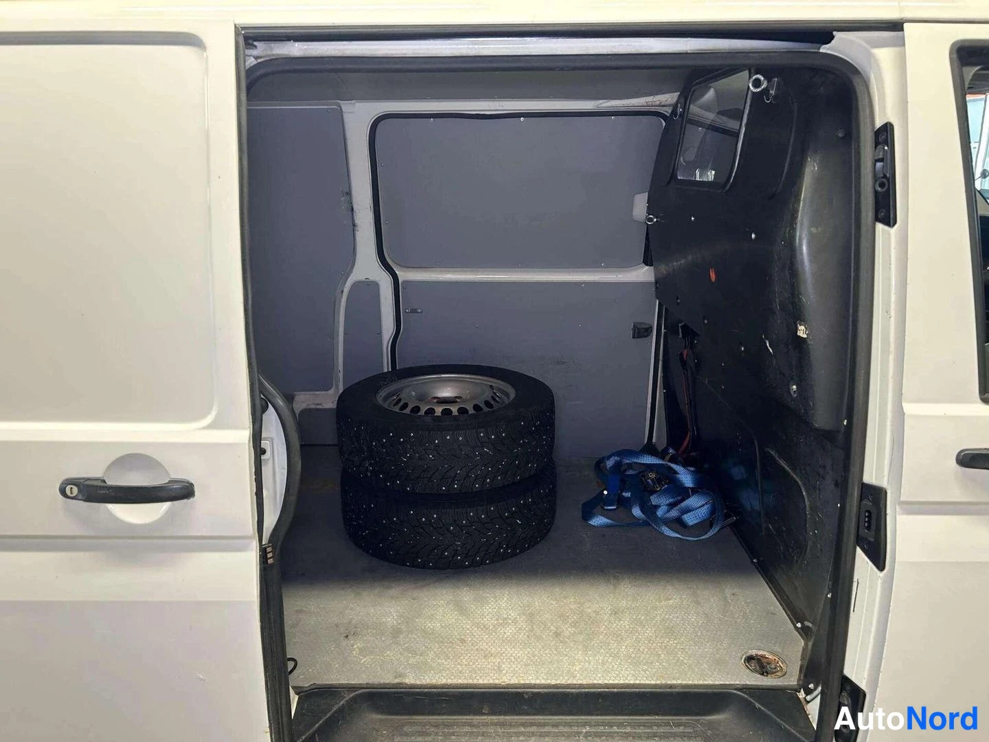 Sivulta: Reklasti avattu pakettiauto: kuormatilassa kaksi nastarengastaa vanteilla, sininen hinaushihna ja hallit mesh. Auto harmaa, kansi valkoinen.