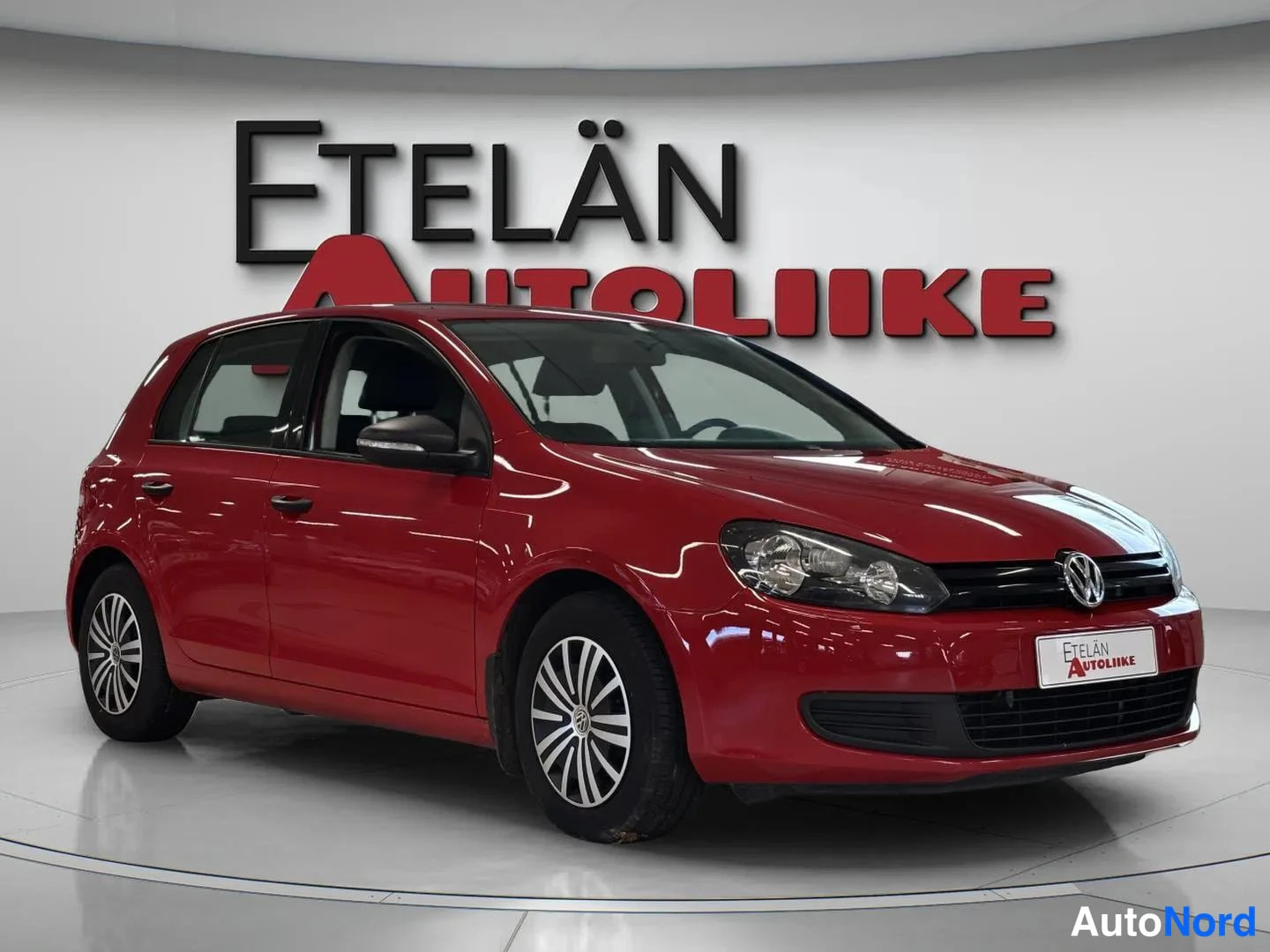 Etuviisto, nokka oikealle: Punainen Volkswagen Golf etukulmasta oikealle, vasen sivu näkyvissä showroomissa.